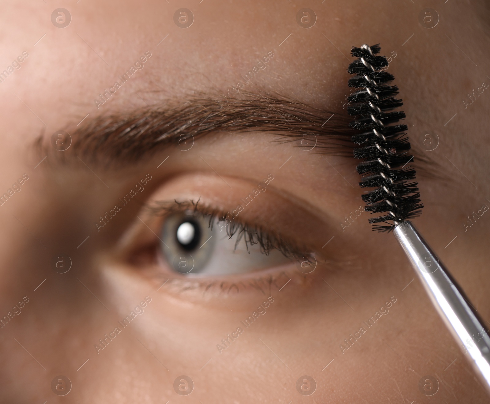 Photo of Young woman brushing her eyebrow with spoolie, closeup