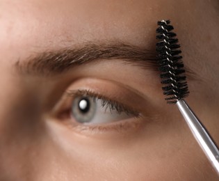 Photo of Young woman brushing her eyebrow with spoolie, closeup