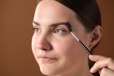 Photo of Young woman brushing her eyebrow with spoolie on brown background, closeup