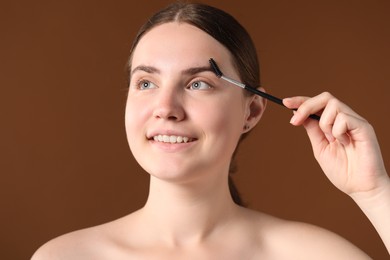 Photo of Young woman brushing her eyebrow with spoolie on brown background