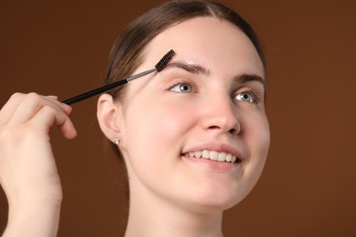Photo of Young woman brushing her eyebrow with spoolie on brown background, closeup