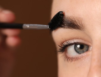 Photo of Young woman brushing her eyebrow with spoolie on brown background, closeup