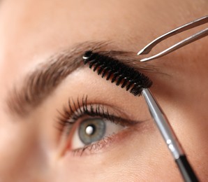 Photo of Plucking and brushing young woman's eyebrow with spoolie, closeup