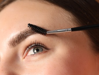 Photo of Young woman brushing her eyebrow with spoolie, closeup