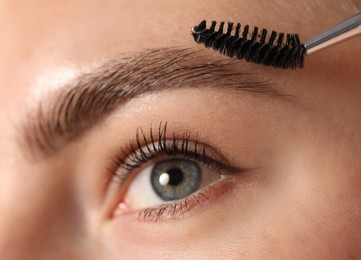 Photo of Young woman brushing her eyebrow with spoolie, closeup
