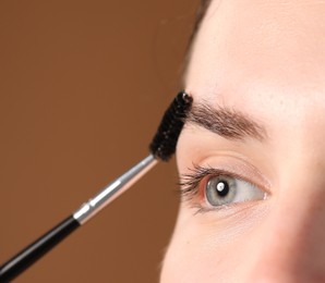 Photo of Young woman brushing her eyebrow with spoolie on brown background, closeup