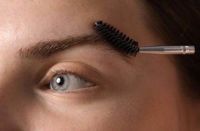 Photo of Young woman brushing her eyebrow with spoolie, closeup