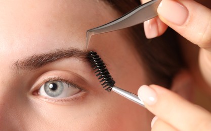 Photo of Cosmetologist plucking and brushing young woman's eyebrow, closeup