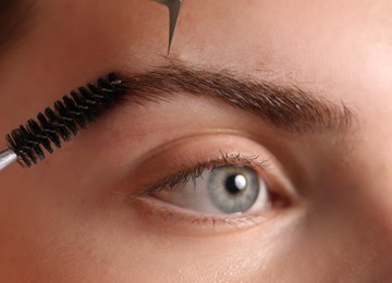 Photo of Cosmetologist plucking and brushing young woman's eyebrow, closeup