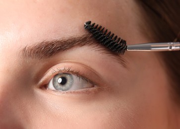 Photo of Young woman brushing her eyebrow with spoolie, closeup