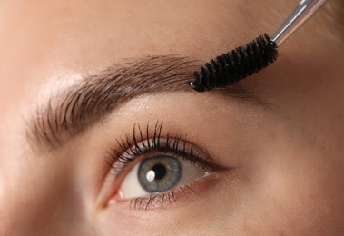 Photo of Young woman brushing her eyebrow with spoolie, closeup