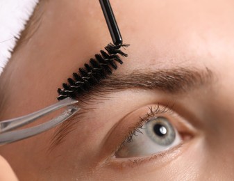Photo of Cosmetologist plucking and brushing young woman's eyebrow, closeup