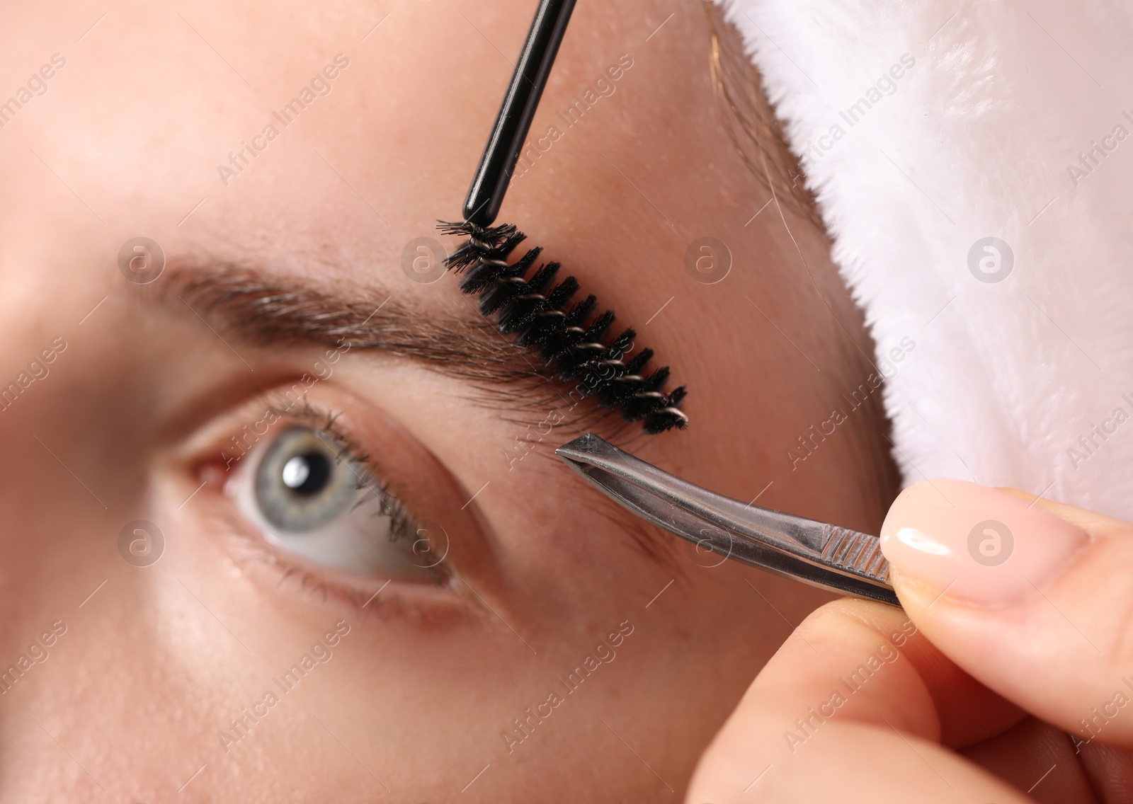 Photo of Cosmetologist plucking and brushing young woman's eyebrow, closeup