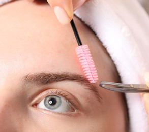 Photo of Cosmetologist plucking and brushing young woman's eyebrow, closeup