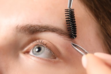 Photo of Cosmetologist plucking and brushing young woman's eyebrow, closeup