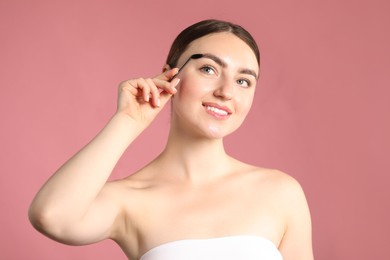 Photo of Young woman brushing her eyebrow with spoolie on pink background