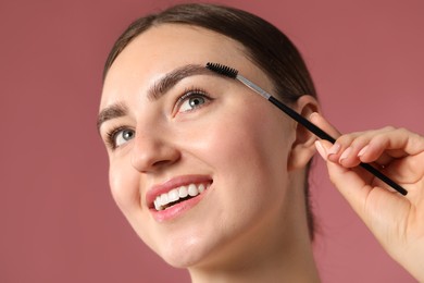 Photo of Young woman brushing her eyebrow with spoolie on pink background, closeup