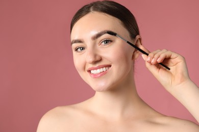Photo of Young woman brushing her eyebrow with spoolie on pink background