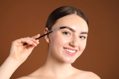 Photo of Young woman brushing her eyebrow with spoolie on brown background