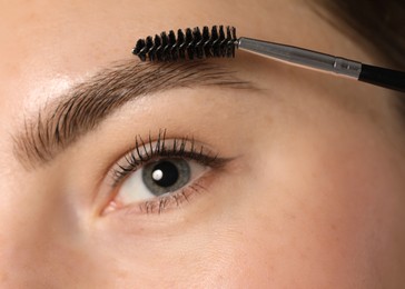 Photo of Young woman brushing her eyebrow with spoolie, closeup