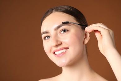 Photo of Young woman brushing her eyebrow with spoolie on brown background