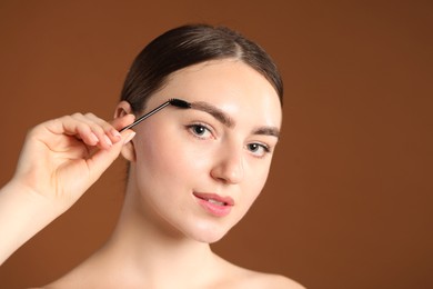 Photo of Young woman brushing her eyebrow with spoolie on brown background