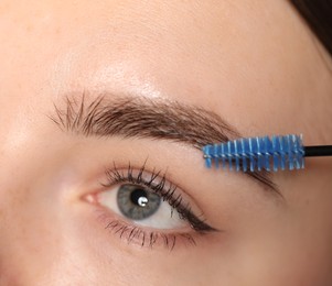 Photo of Young woman brushing her eyebrow with spoolie, closeup