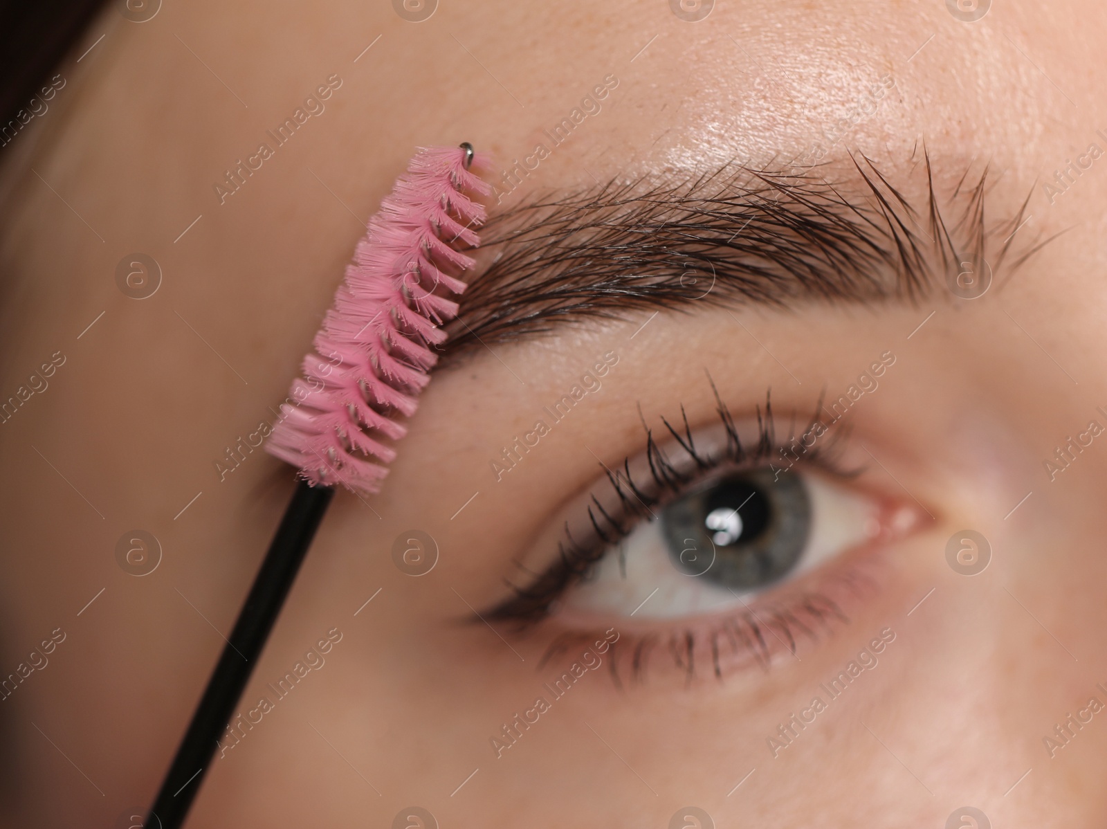 Photo of Young woman brushing her eyebrow with spoolie, closeup