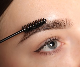 Photo of Young woman brushing her eyebrow with spoolie, closeup