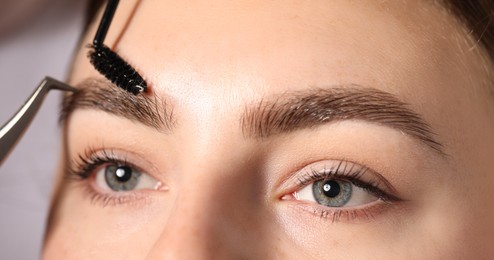 Photo of Plucking and brushing young woman's eyebrow with spoolie on light grey background, closeup