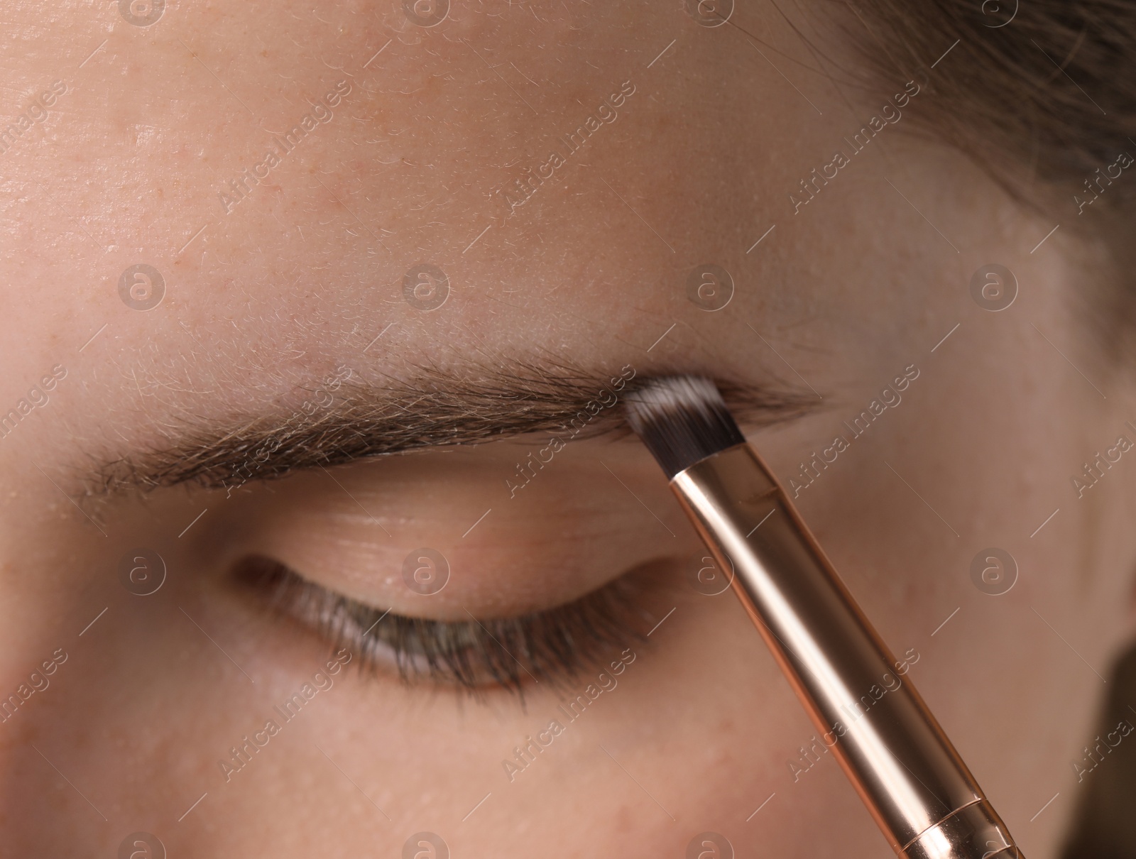 Photo of Young woman applying cosmetic product onto her eyebrow with brush, closeup