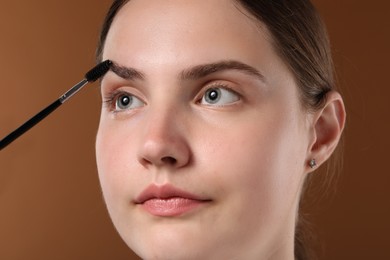 Photo of Young woman brushing her eyebrow with spoolie on brown background, closeup