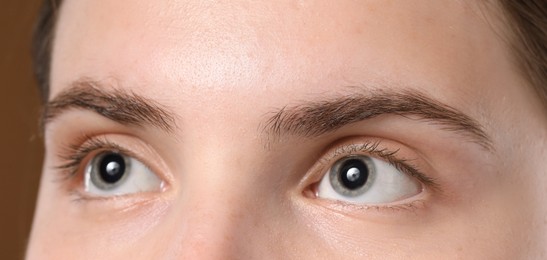 Photo of Young woman with beautiful eyebrows on brown background, closeup