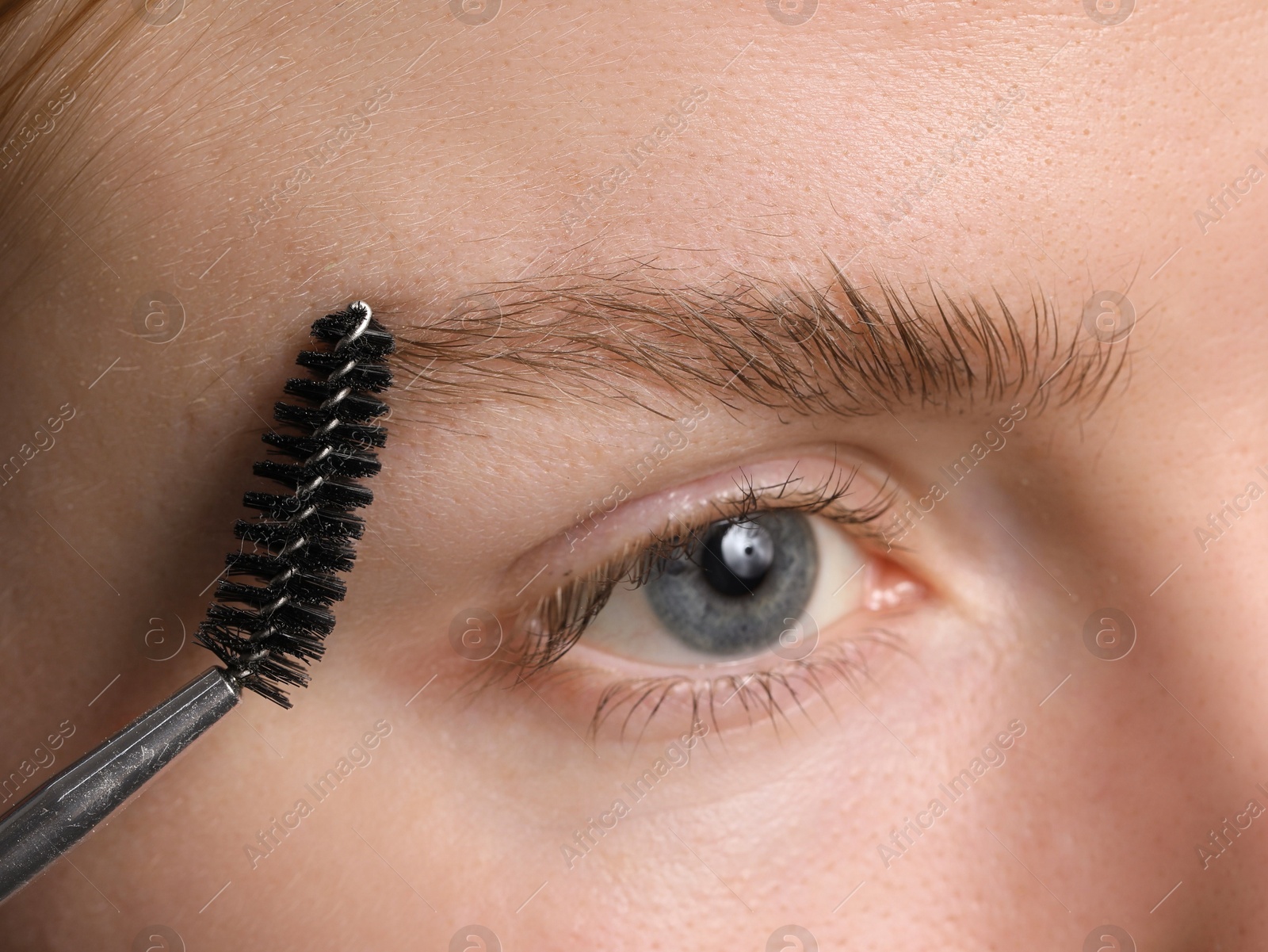 Photo of Young woman brushing her eyebrow with spoolie, closeup