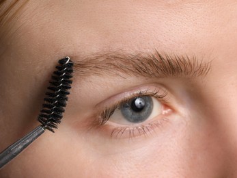 Photo of Young woman brushing her eyebrow with spoolie, closeup