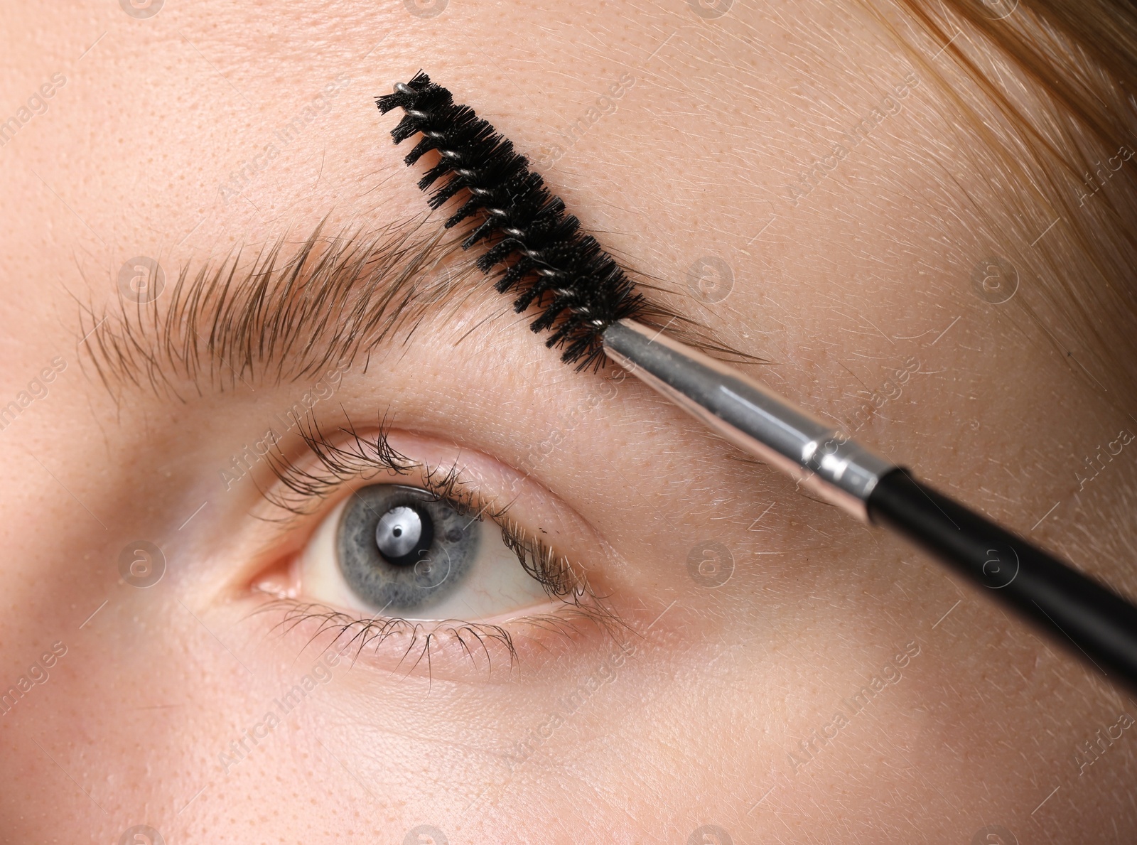 Photo of Young woman brushing her eyebrow with spoolie, closeup