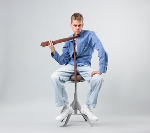 Photo of Handsome young man wearing stylish clothes sitting on chair against light grey background