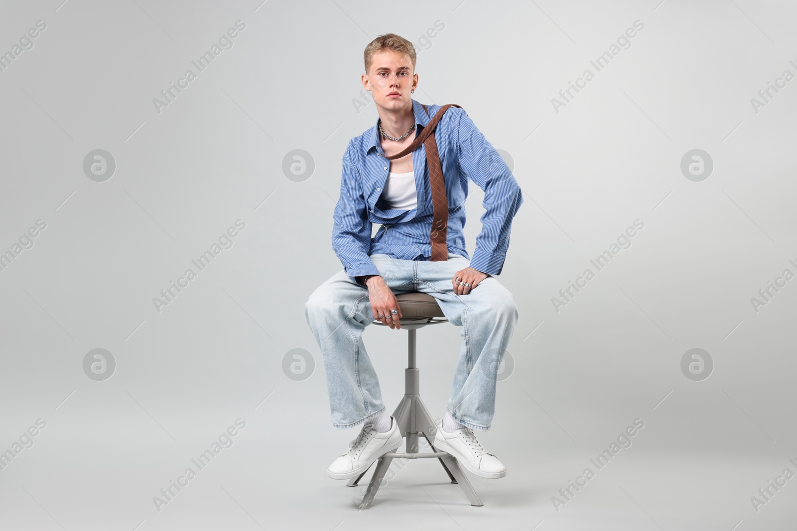 Photo of Handsome young man wearing stylish clothes sitting on chair against light grey background