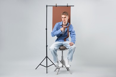 Photo of Handsome young man wearing stylish clothes sitting on chair against light grey background