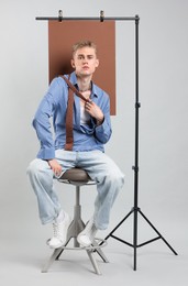 Photo of Handsome young man wearing stylish clothes sitting on chair against light grey background