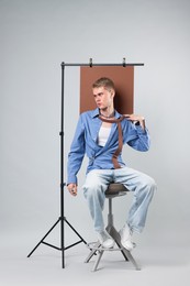 Photo of Handsome young man wearing stylish clothes sitting on chair against light grey background