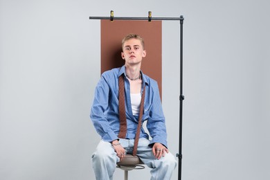 Photo of Handsome young man wearing stylish clothes sitting on chair against light grey background