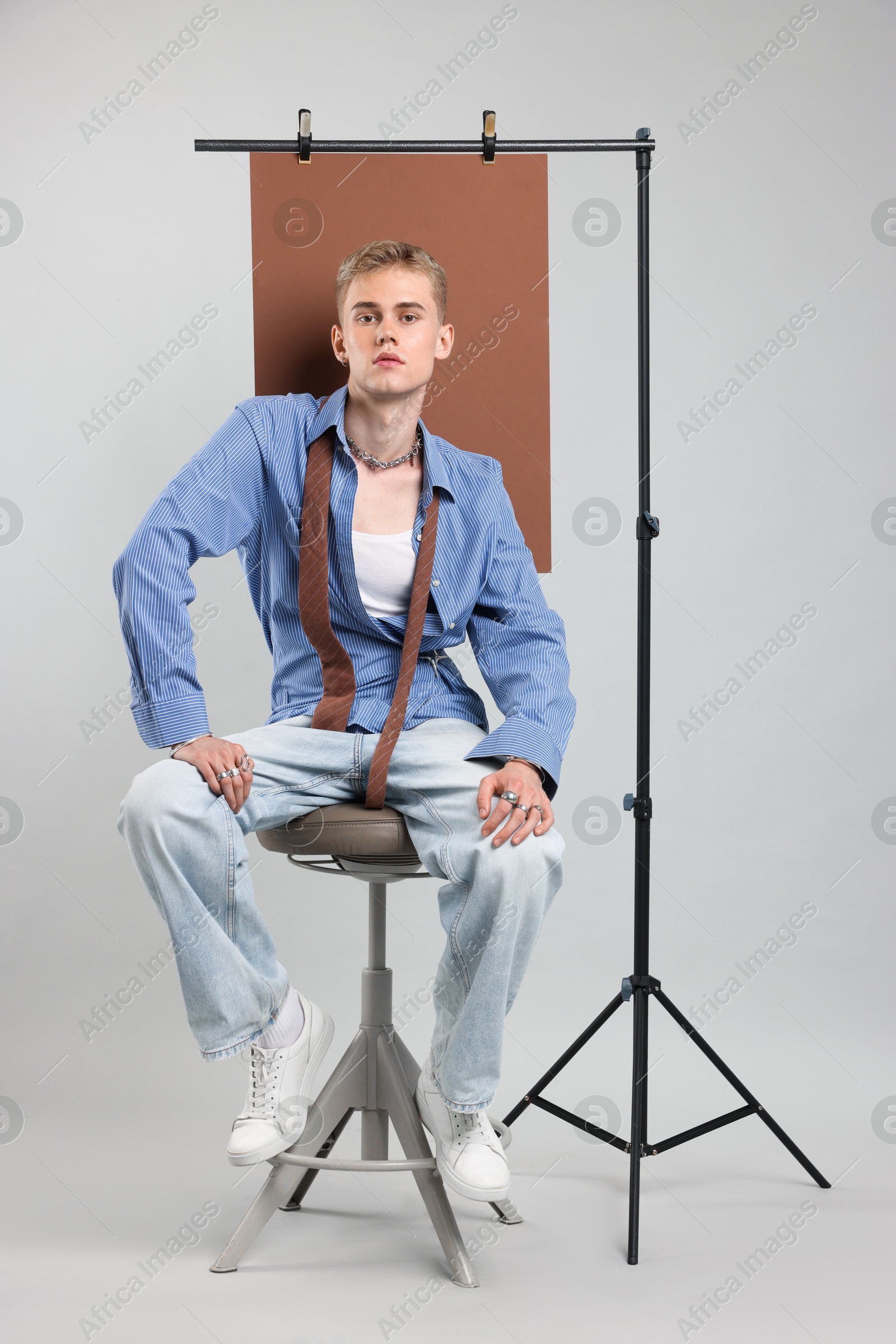 Photo of Handsome young man wearing stylish clothes sitting on chair against light grey background