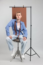 Photo of Handsome young man wearing stylish clothes sitting on chair against light grey background