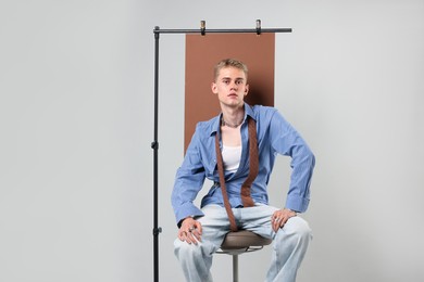 Photo of Handsome young man wearing stylish clothes sitting on chair against light grey background