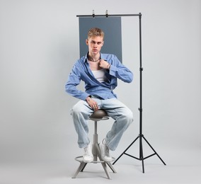 Photo of Handsome young man wearing stylish clothes sitting on chair against light grey background