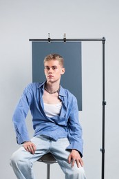 Photo of Handsome young man wearing stylish clothes sitting on chair against light grey background
