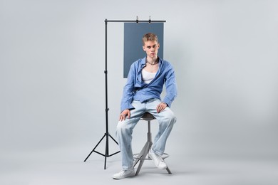 Photo of Handsome young man wearing stylish clothes sitting on chair against light grey background
