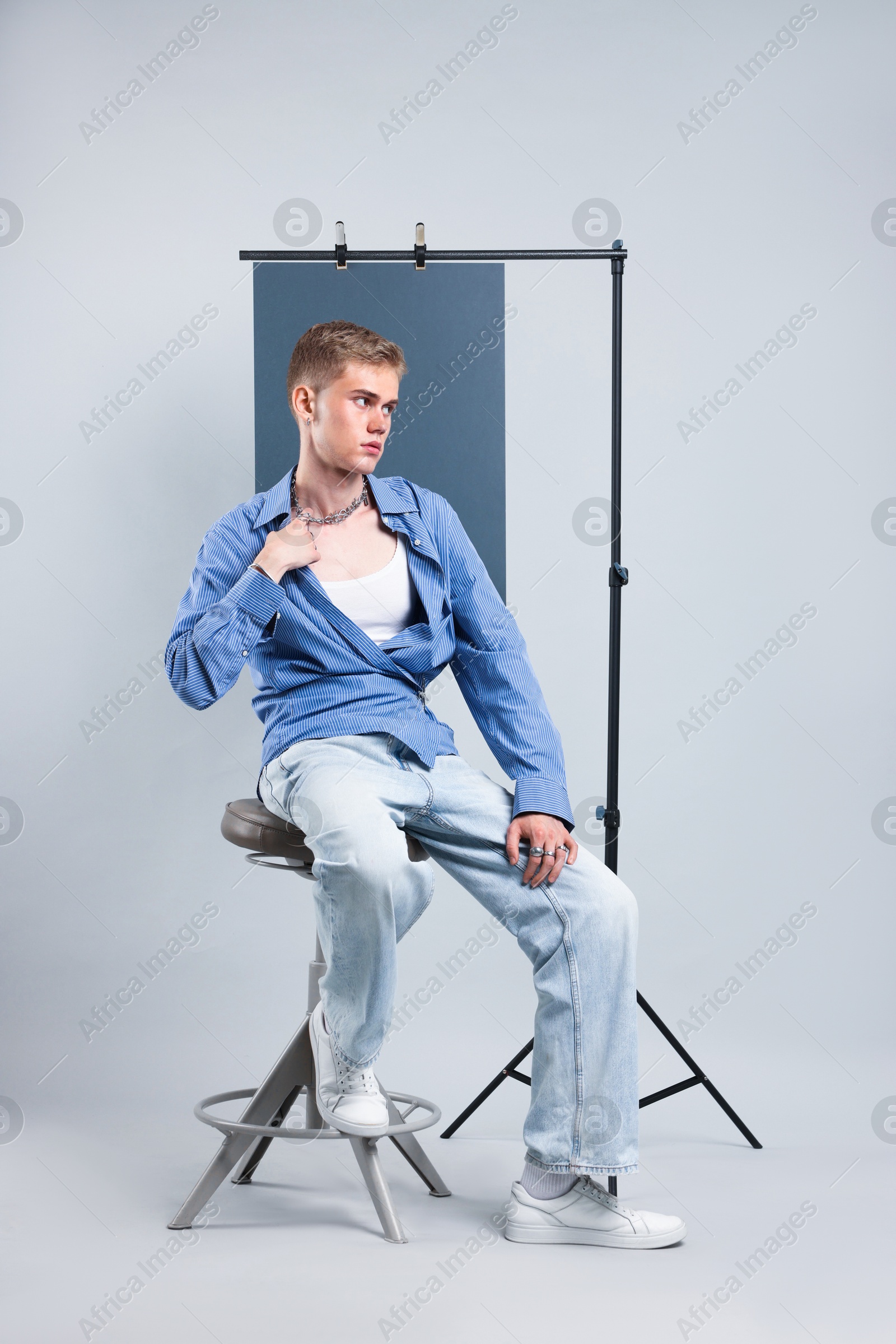 Photo of Handsome young man wearing stylish clothes sitting on chair against light grey background