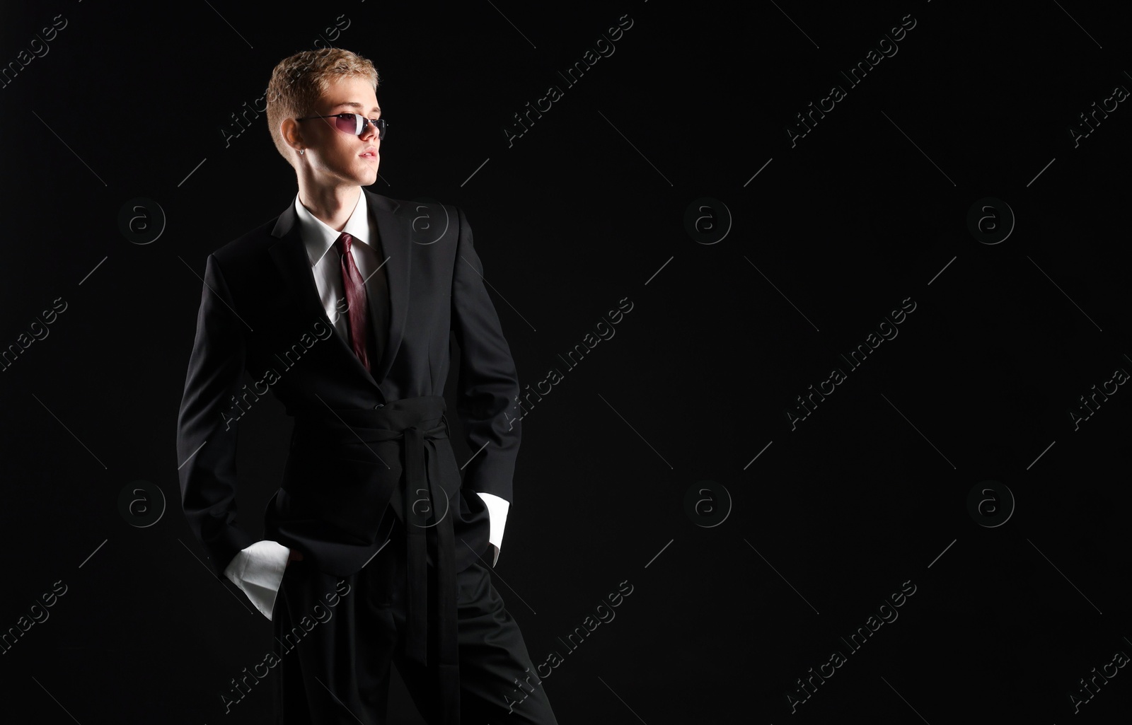 Photo of Handsome young man wearing stylish suit and sunglasses on black background, space for text